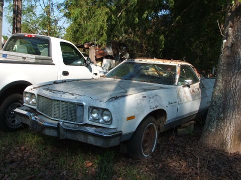 1966 Ford Ranchero - This 1977 Ford Ranchero shows significant rust and peeling paint, parked beside a modern pickup truck.