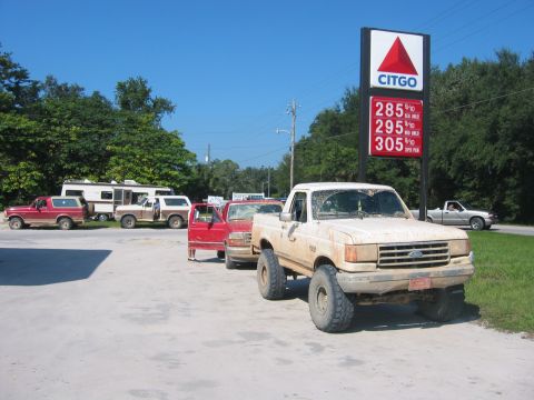 1989 Ford Bronco - Several Ford Broncos, an RV, and a pickup truck are lined up at a gas station on a sunny day.