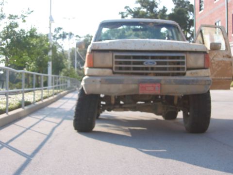 1989 Ford Bronco - A muddy Ford truck is parked with the driver's door ajar, showing its front grille and tires.