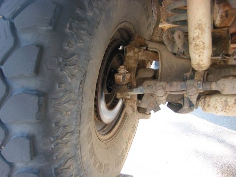 1989 Ford Bronco - This image shows the front wheel suspension and tire of a vehicle, with visible rust and dirt on the components.