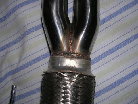 1996 Ford Probe - A close-up view of a shiny exhaust header pipe, likely an aftermarket part, with a braided flex pipe section.