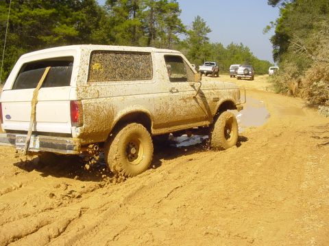 1989 Ford Bronco - This SUV is navigating a challenging muddy terrain, with other vehicles following in the distance.