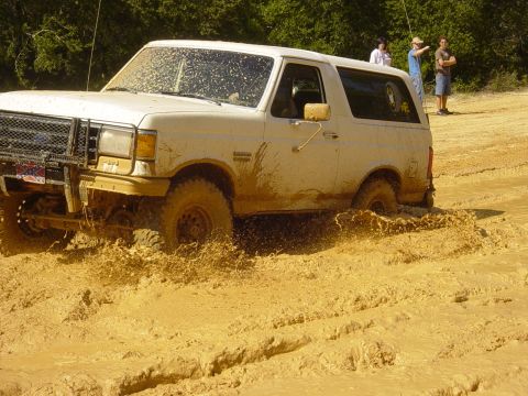 1989 Ford Bronco - A white 1987 Ford Bronco navigates a muddy terrain, with people watching in the background.