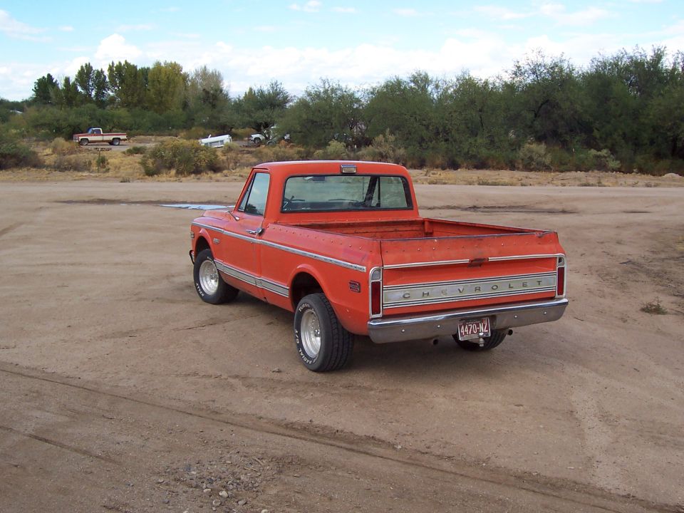 Orange pickup truck, rear 3/4 view, in a dirt lot. Chrome bumper, "CHEVROLET" tailgate