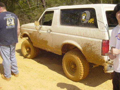 1989 Ford Bronco - A muddy 1989 Ford Bronco sits off-road, with two onlookers present.