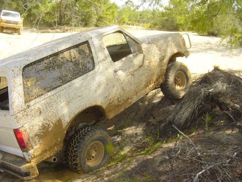 1989 Ford Bronco - This SUV is covered in mud while navigating an off-road trail, with another vehicle visible in the distance.