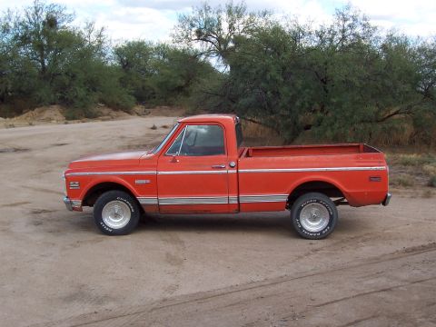 1972 Chevrolet C/K Pickup - This orange pickup truck, likely from the early 1970s, is seen from the side on a dusty, unpaved surface.