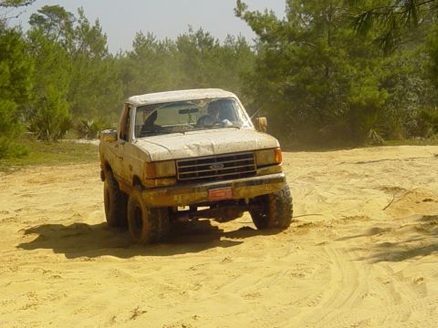 1989 Ford Bronco - This lifted pickup truck navigates a sandy terrain, kicking up dust as it goes.
