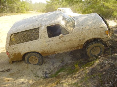 1989 Ford Bronco - Muddy 1989 Ford Bronco struggling on a dirt incline, with a second vehicle visible in the background.