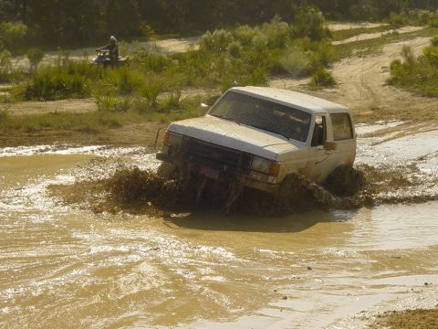 1989 Ford Bronco - White 1989 Ford Bronco navigates a muddy off-road course, splashing through water.