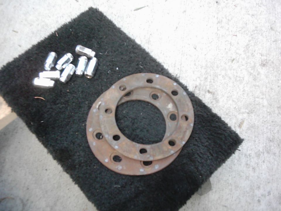 Bunch of lug nuts and two rusty brake rotors on a black mat