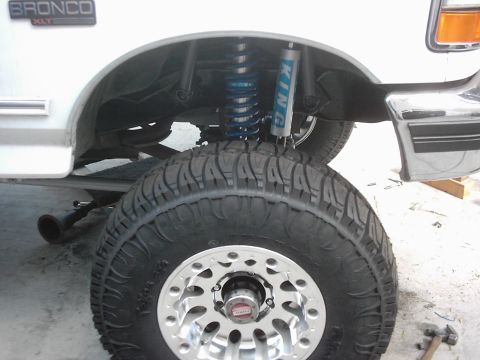 1978 Ford Bronco - Close-up of a white Ford Bronco's fender well, a large off-road tire and blue King shocks.