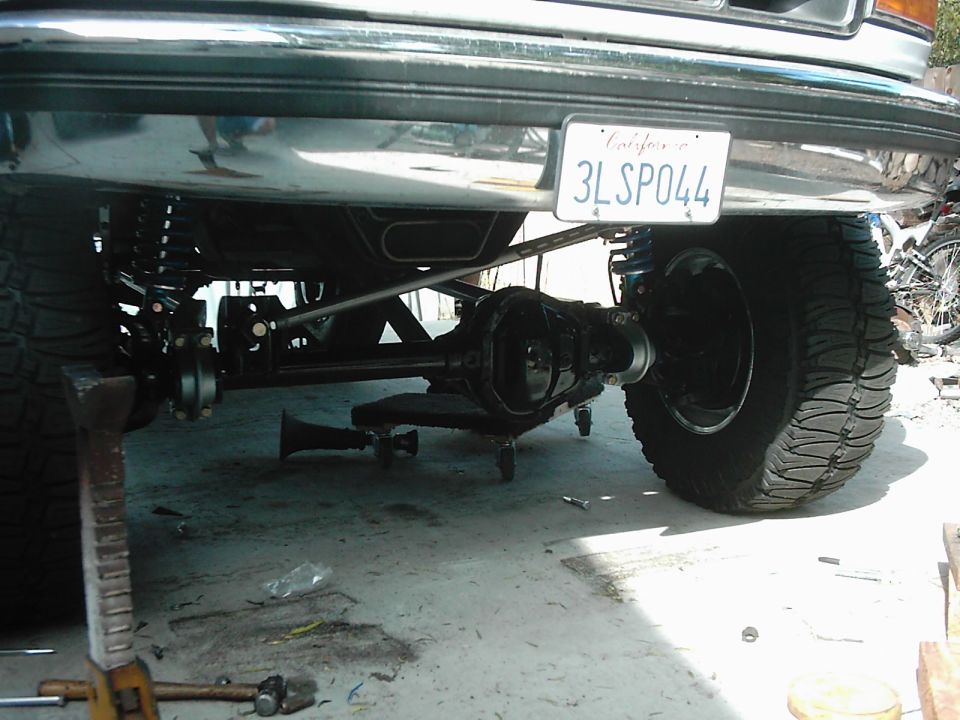 Underneath view of a lifted truck's rear axle, suspension, and tires. California license plate 3LSP044 is visible