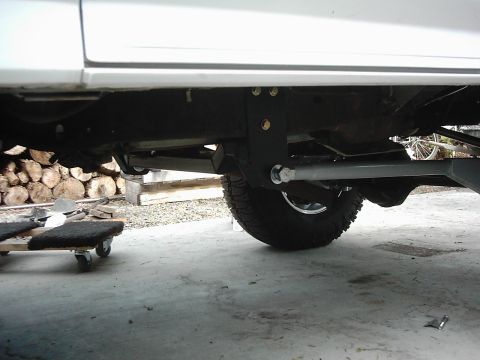 1978 Ford Bronco - This photo shows the undercarriage of a vehicle, focusing on the suspension and tire, with a pile of logs in the background.