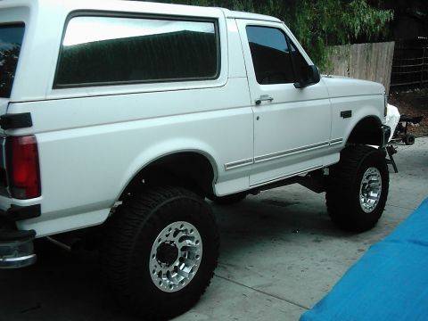 1978 Ford Bronco - This white SUV is shown from a 3q-front angle, highlighting its lifted suspension and large off-road tires.