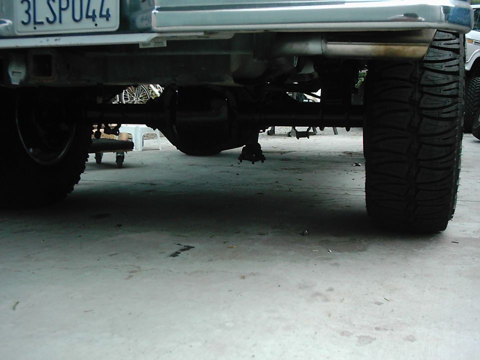 Rear axle, suspension, and large tire of a vehicle. A license plate is visible