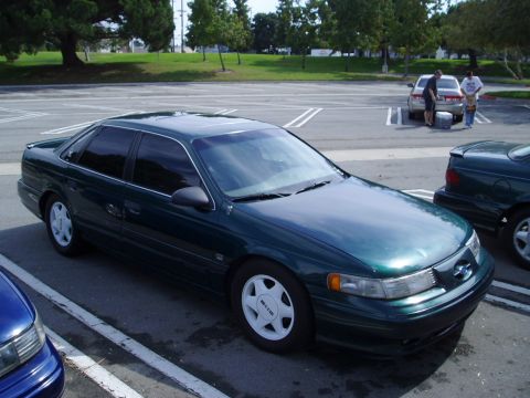 1993 Ford Taurus - A dark green 1993 Ford Taurus sedan is parked in a lot with other vehicles.