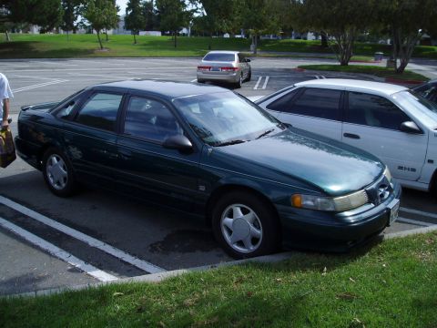 1993 Ford Taurus - A dark green 1993 Ford Taurus is parked in a lot, with another car visible to its right.