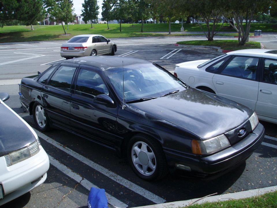 Black sedan parked in a lot, front quarter view. Scratched paint on roof