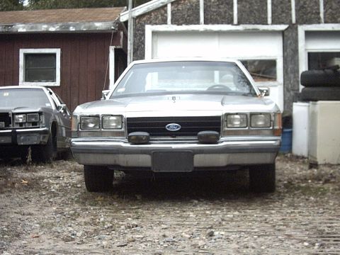 1991 Ford Crown Victoria LTD - Front view of a 1991 Ford Crown Victoria LTD parked outside a garage with another vehicle nearby.