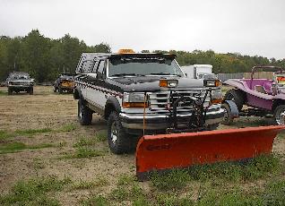 1979 Ford Bronco - A black and white Ford F-series truck is equipped with a large orange plow and parked in a lot with other vehicles.