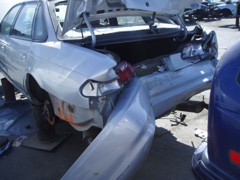 1993 Ford Taurus - The rear of a damaged silver sedan is shown, with its trunk open and bumper hanging off.