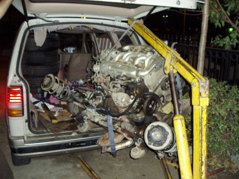 1993 Ford Taurus - Engine and suspension components are being loaded into the rear of a van using a yellow engine hoist.