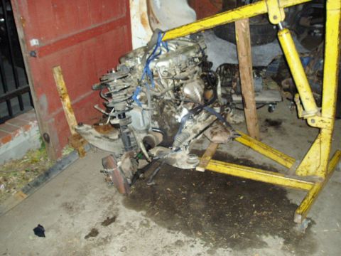 1993 Ford Taurus - Engine and subframe assembly, likely removed from a vehicle, is supported by an engine hoist.