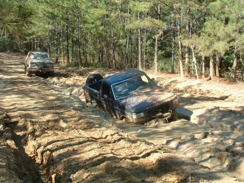 1993 Ford Bronco - Two trucks navigate a muddy off-road trail with one vehicle deeply mired.
