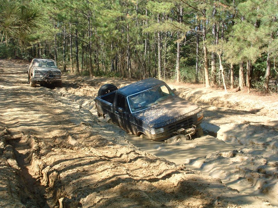 Black Ford F-Series truck stuck in mud, spare tire in bed