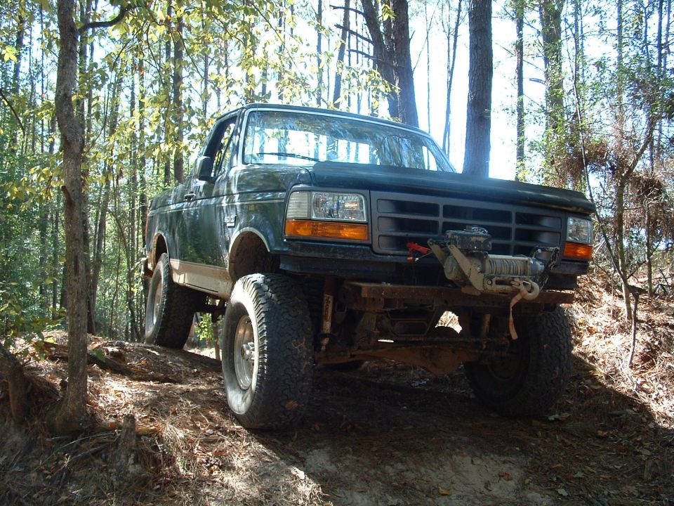 Dark green lifted Ford truck with winch, off-road tires, and aftermarket bumper