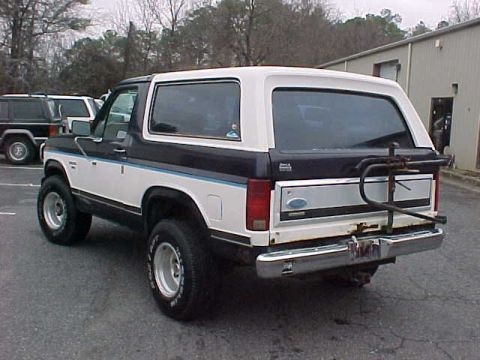 1985 Ford Bronco - A two-tone Ford Bronco is parked in a lot with other vehicles.