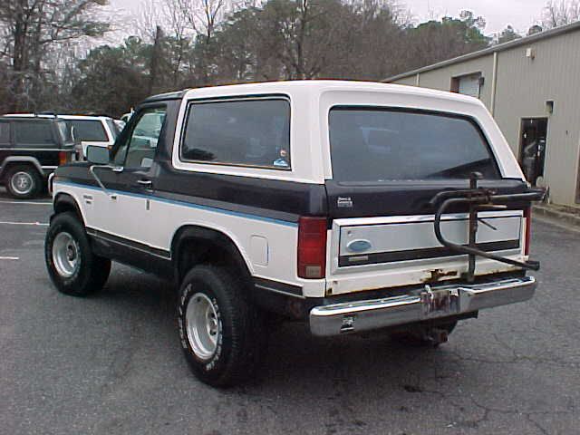 Two-tone Ford Bronco with a bike rack on the rear, parked next to other SUVs