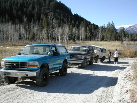 1994 Ford Bronco - Three Ford Broncos are parked on a dirt road in a wooded area. The lead vehicle is teal.