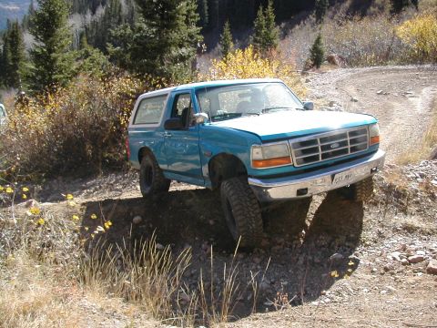 1994 Ford Bronco - A blue Ford Bronco navigates a rough, off-road trail during autumn.