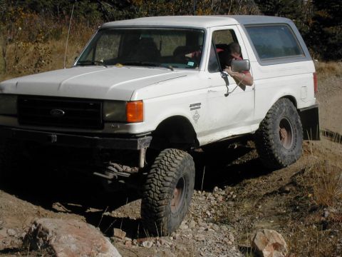 1994 Ford Bronco - A white Ford Bronco navigates a rough, off-road path with large tires.