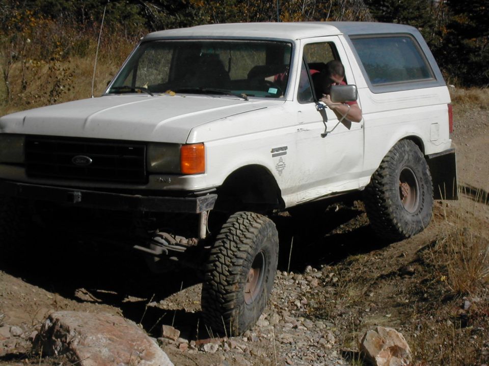 White Ford Bronco with lifted suspension driving on a rocky trail