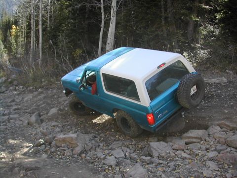 1994 Ford Bronco - This Ford Bronco is shown on a challenging, rocky off-road path with trees in the background.