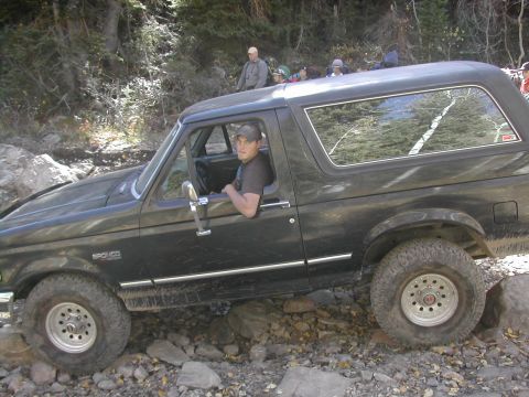 1994 Ford Bronco - A driver navigates a black 1994 Ford Bronco over a challenging, rocky off-road path.
