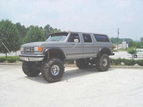 1986 Ford Bronco - This lifted SUV, likely a 1987 model based on its grille, is shown from a three-quarter front angle.