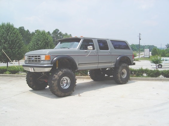 Gray lifted four-door SUV with large tires, parked on concrete. Visible grille and side profile