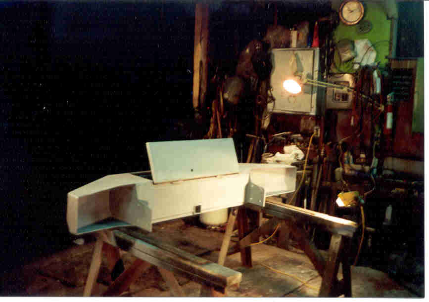 White fiberglass part on sawhorses in a workshop with tools and equipment in the background