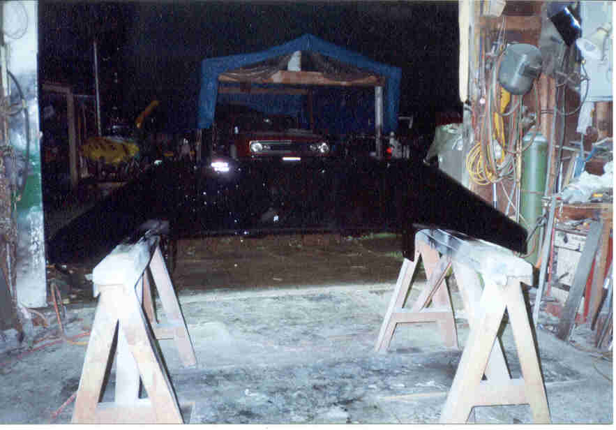 Black fabricated truck bumper on wooden sawhorses in a dim workshop