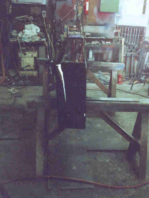 Black panel, possibly a door or fender, on wooden sawhorses in a workshop