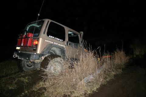 2003 Jeep TJ - A Jeep Wrangler is stuck on a muddy trail at night, with tall grass obscuring the tires.