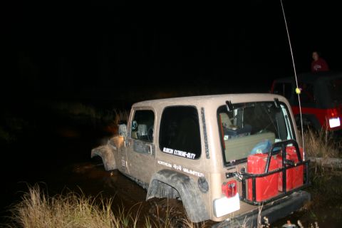 2003 Jeep TJ - Two Jeep Wranglers are stuck in the mud at night, one tan and one red.