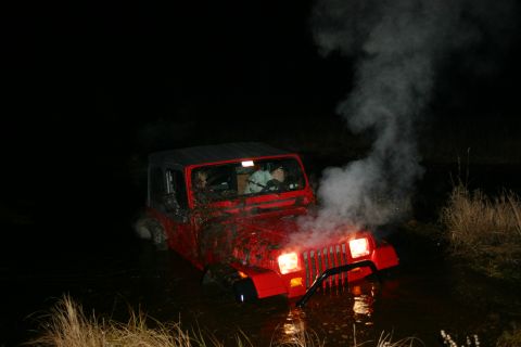 2003 Jeep TJ - Red 2003 Jeep TJ stuck in mud and water at night, with smoke billowing from the hood.