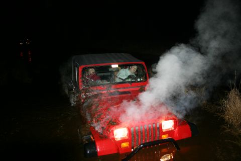 2003 Jeep TJ - A red Jeep Wrangler appears to be stuck in mud at night, with steam billowing from its hood.