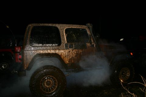 2003 Jeep TJ - A muddy Jeep Wrangler emits exhaust smoke at night, with another vehicle nearby.