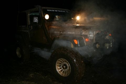2003 Jeep TJ - A muddy 2003 Jeep TJ is seen at night, equipped with a snorkel and off-road lights, kicking up smoke.